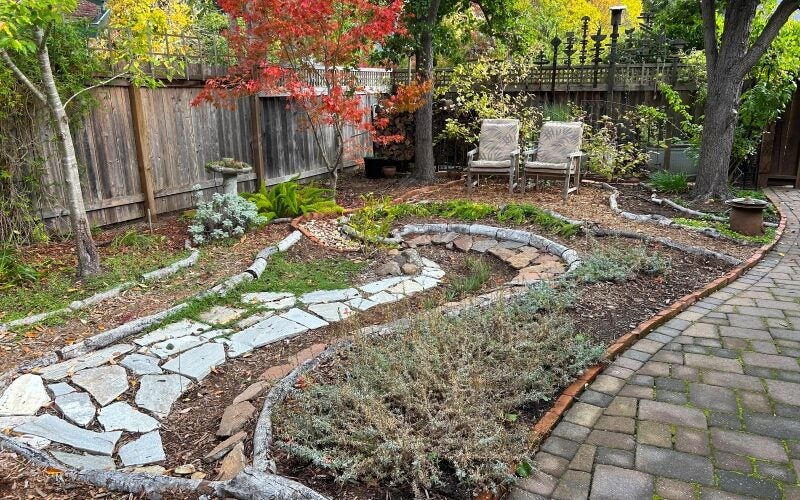 Pavers create a meandering rain garden lined with vibrant plants in this backyard