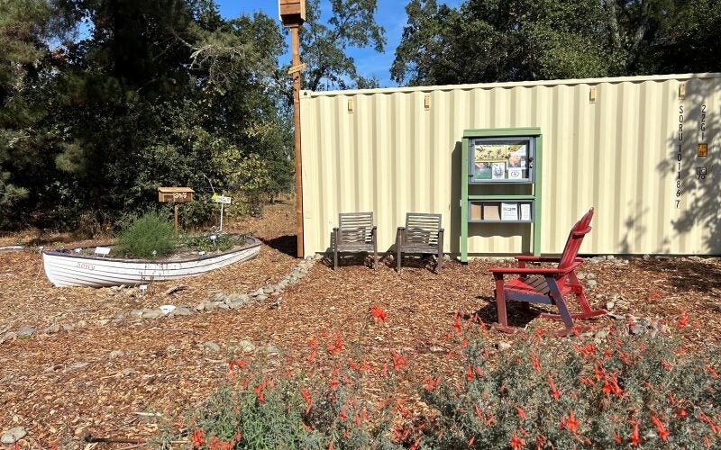 A sitting area with an old wooden boat turned into a planter and a small library box